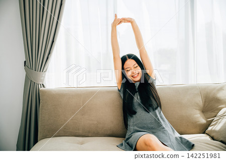 Smiling woman in luxury living room raises arms stretches after sitting Smiling woman in luxury living room raises arms stretches after sitting 142251981