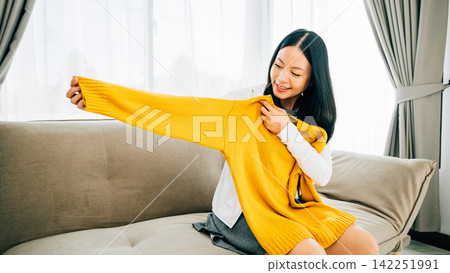 Happy Asian woman reveals a shirt from a box smiling with delight at home Happy Asian woman reveals a shirt from a box smiling with delight at home 142251991