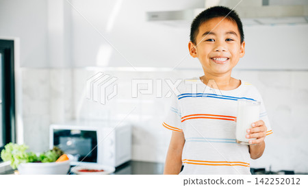 Portrait of smiling Asian little boy in kitchen holding milk. Cute son enjoys drink, radiating joy. Young child savoring calcium-rich liquid, feeling happy at home give me. Portrait of smiling Asian little boy in kitchen holding milk. Cute son enjoys drink, radiating joy. Young child savoring calcium-rich liquid, feeling happy at home give me. 142252012