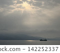 A calm sea and ship bathed in light filtering through the clouds. 142252337