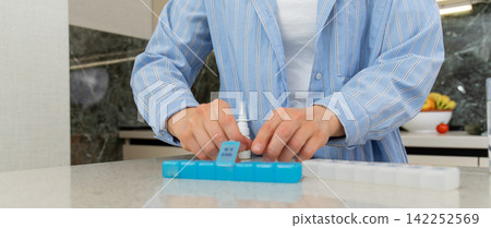 Woman methodically fills pill organizer with vitamins and supplements Woman methodically fills pill organizer with vitamins and supplements 142252569