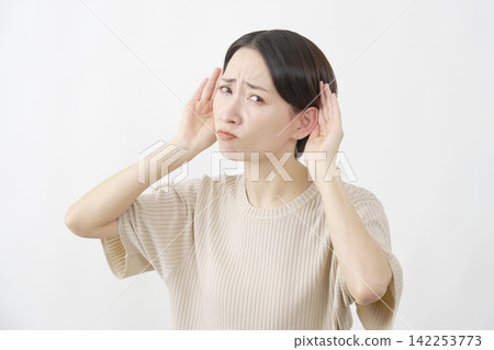 一名女子將手放在耳朵上，試圖聽清楚聲音，背景是白色的。 142253773