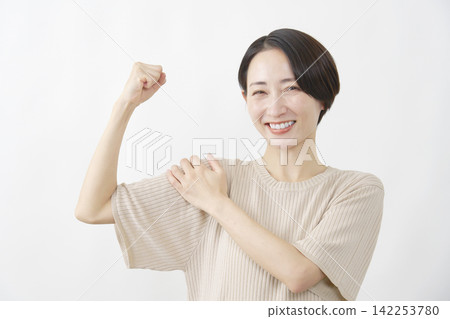 A smiling woman, middle-aged, flexing her bicep; wearing white. A smiling woman, middle-aged, flexing her bicep; wearing white. 142253780