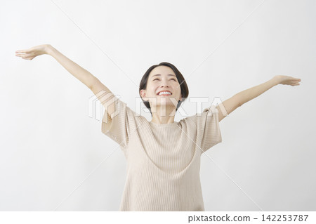 A woman takes a deep breath with her arms outstretched against a white background. A woman takes a deep breath with her arms outstretched against a white background. 142253787