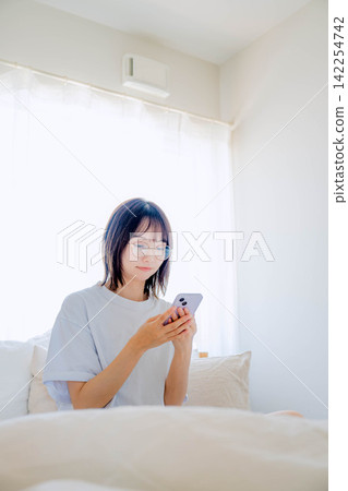 一名女子在臥室床上使用智慧型手機。 142254742