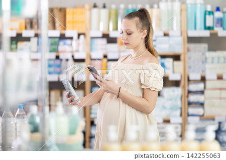 Young pregnant woman scanning QR-code on cream in drugstore Young pregnant woman scanning QR-code on cream in drugstore 142255063