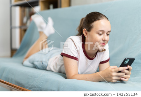 Teenage girl scrolling social media feed on sofa Teenage girl scrolling social media feed on sofa 142255134
