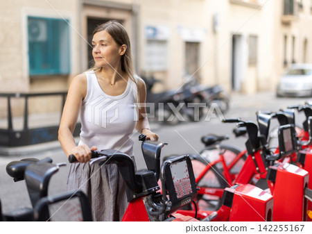 Woman rents bicycle, starts journey at parking lot Woman rents bicycle, starts journey at parking lot 142255167