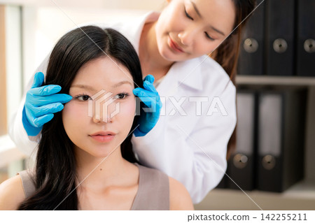 Young asian woman aesthetic doctor examining face of woman patient in clinical office. Young asian woman aesthetic doctor examining face of woman patient in clinical office. 142255211