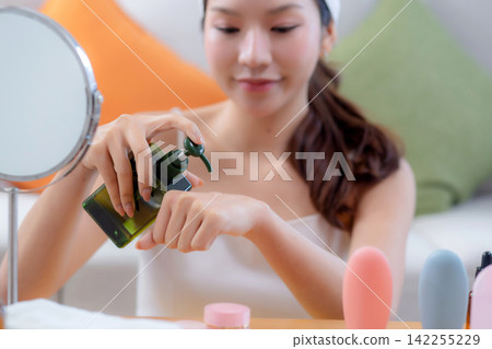 Beautiful young asian woman applying lotion herb on hands looking mirror at home. 142255229