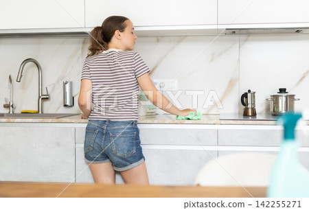 Teenage girl cleans cupboards and furniture in kitchen Teenage girl cleans cupboards and furniture in kitchen 142255271