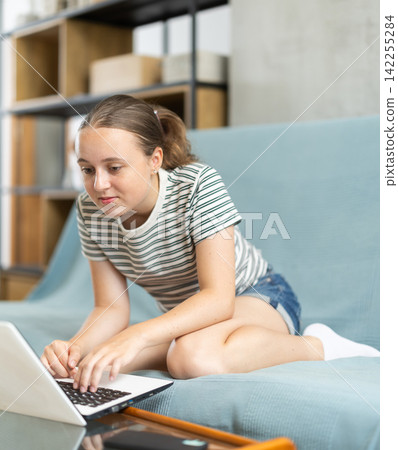 Girl works with laptop in living room on sofa Girl works with laptop in living room on sofa 142255284