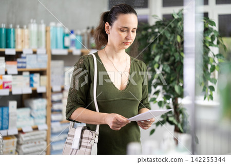 Middle-aged woman looking for medicaments according to prescription Middle-aged woman looking for medicaments according to prescription 142255344