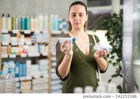 Middle-aged woman customer choosing ointment in box in drugstore Middle-aged woman customer choosing ointment in box in drugstore 142255386