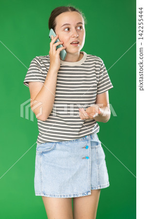 Teenage girl talking on mobile phone in front of green screen 142255444