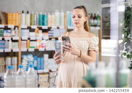 Young pregnant woman in pharmacy scans QR code on soothing body balm Young pregnant woman in pharmacy scans QR code on soothing body balm 142255459