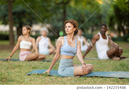 Woman stretching in lotus position during group yoga in park Woman stretching in lotus position during group yoga in park 142255486