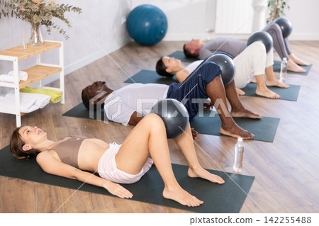 Active women and men doing pilates with soft ball lying on back in gym 142255488