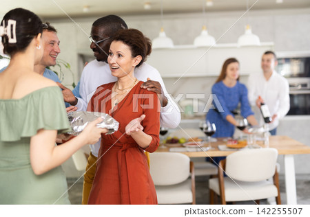Smiling couple greeting guests bearing dish for friendly party Smiling couple greeting guests bearing dish for friendly party 142255507