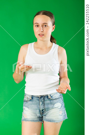 Portrait of european teen girl dressed in stylish shorts standing against green background talking with gesturing energetically and giving examples Portrait of european teen girl dressed in stylish shorts standing against green background talking with gesturing energetically and giving examples 142255510