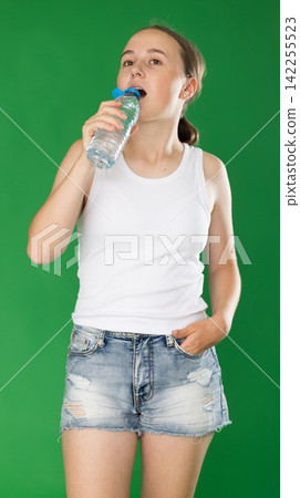 Teenage girl drinking water in front of green screen Teenage girl drinking water in front of green screen 142255523