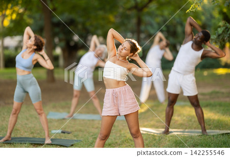 Girl doing Swaying Palm Pose at group yoga class in park Girl doing Swaying Palm Pose at group yoga class in park 142255546