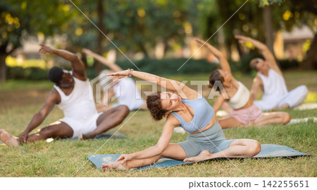 Multinational yoga enthusiasts with female coach perform Janu Shirshasana in park Multinational yoga enthusiasts with female coach perform Janu Shirshasana in park 142255651