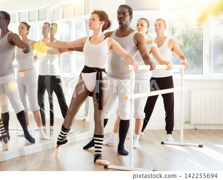 Woman practicing battement tendu at barre during ballet group class Woman practicing battement tendu at barre during ballet group class 142255694