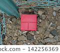 Red boundary markers embedded in the gravel area along the wire mesh fence. 142256369