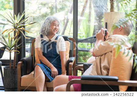 Asian senior couple enjoying a photographing session in a cozy setting during their journey. Asian senior couple enjoying a photographing session in a cozy setting during their journey. 142256522