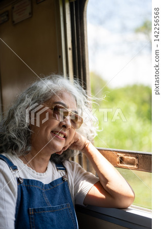 Asian senior elderly woman enjoying the scenery from a vintage train window during a solo trip. Asian senior elderly woman enjoying the scenery from a vintage train window during a solo trip. 142256568