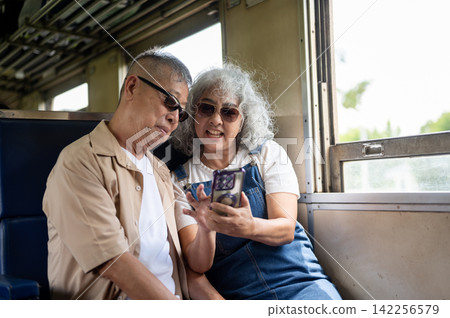 Asian senior elderly couple looking at smartphone together while enjoying their vintage train trip. Asian senior elderly couple looking at smartphone together while enjoying their vintage train trip. 142256579