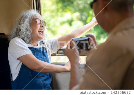 Asian senior woman laughing while photographing scenery during a train journey Asian senior woman laughing while photographing scenery during a train journey 142256682