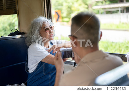 Asian senior elderly couple sharing a pleasant conversation with her partner during a train ride. Asian senior elderly couple sharing a pleasant conversation with her partner during a train ride. 142256683