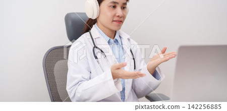 Professional doctor wearing headphone and lab coat using laptop for telehealth, telemedicine, online consultation and medical technology video meeting at desk in hospital office concept Professional doctor wearing headphone and lab coat using laptop for telehealth, telemedicine, online consultation and medical technology video meeting at desk in hospital office concept 142256885