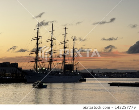 The silhouette of a sailing ship and its mast against the orange sky before sunrise. The silhouette of a sailing ship and its mast against the orange sky before sunrise. 142257779