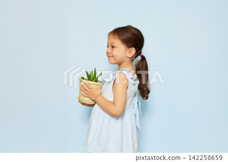 Young girl smiling and carrying a small green houseplant, representing growth, care, and connection with nature Young girl smiling and carrying a small green houseplant, representing growth, care, and connection with nature 142258659