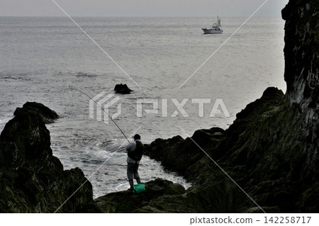 At dusk, the silhouettes of fishing boats and anglers fishing from the rocky shore of Manazuru. 142258717