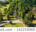 Aerial view of Herrenkrug in Magdeburg shows tree-lined avenue beside tram tracks, park lawns and station shelter. Summer landscape combines public transport, greenery and quiet urban recreation 142258960
