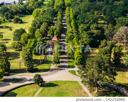 Aerial view of Herrenkrug in Magdeburg shows tree-lined avenue beside tram tracks, park lawns and station shelter. Summer landscape combines public transport, greenery and quiet urban recreation Aerial view of Herrenkrug in Magdeburg shows tree-lined avenue beside tram tracks, park lawns and station shelter. Summer landscape combines public transport, greenery and quiet urban recreation 142258960