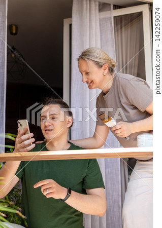 Middle aged man shows information on a smartphone while a woman paints a handmade wooden shelf with a brush during a DIY project. Concept of digital learning, teamwork, woodworking and home Middle aged man shows information on a smartphone while a woman paints a handmade wooden shelf with a brush during a DIY project. Concept of digital learning, teamwork, woodworking and home 142259074