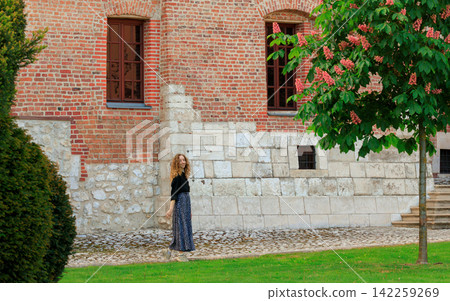 Young woman with curly hair smiles in a garden with blooming chestnut tree 142259269