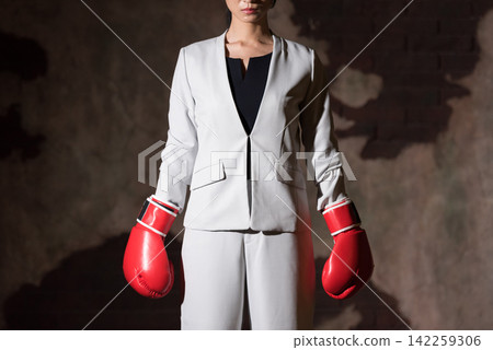 Business woman wearing fighting pose with boxing gloves Business woman wearing fighting pose with boxing gloves 142259306