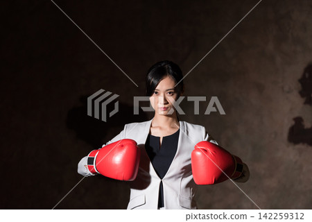 Business woman wearing fighting pose with boxing gloves Business woman wearing fighting pose with boxing gloves 142259312
