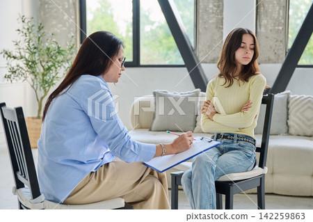 Offended young woman sitting with crossed arms near female psychologist Offended young woman sitting with crossed arms near female psychologist 142259863