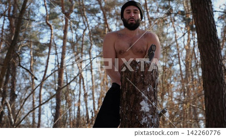 Muscular bearded guy chopping firewood in sunny winter forest. Shirtless young man working with axe in snowy woodland. Concept of strength, masculine, energy and harmony with nature during cold season Muscular bearded guy chopping firewood in sunny winter forest. Shirtless young man working with axe in snowy woodland. Concept of strength, masculine, energy and harmony with nature during cold season 142260776