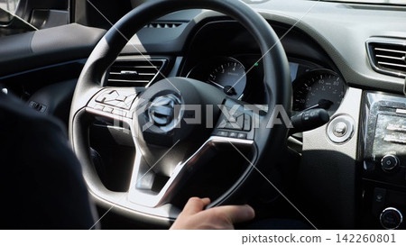 Male arms holds steering wheel while driving a motor car at city. Young man operating the automobile at urban road. Driver moving in his auto on route. Slow motion Male arms holds steering wheel while driving a motor car at city. Young man operating the automobile at urban road. Driver moving in his auto on route. Slow motion 142260801