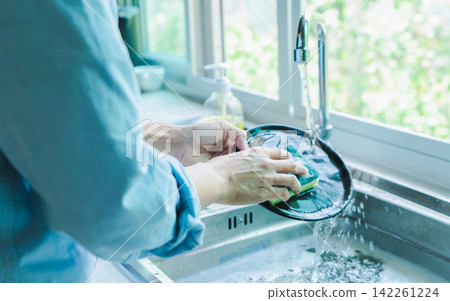 Close-up of a woman washing dishes with dirty food scraps Cleaner in the sink the kitchen counter at home. Close-up of a woman washing dishes with dirty food scraps Cleaner in the sink the kitchen counter at home. 142261224