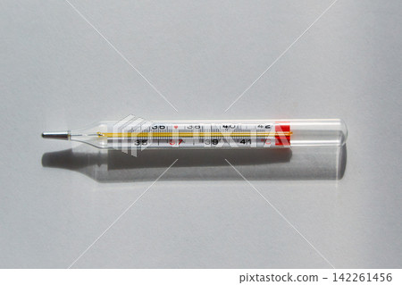 Glass Clinical Thermometer Lying on White Surface Showing Body Temperature and Medical Measurement Scale Glass Clinical Thermometer Lying on White Surface Showing Body Temperature and Medical Measurement Scale 142261456