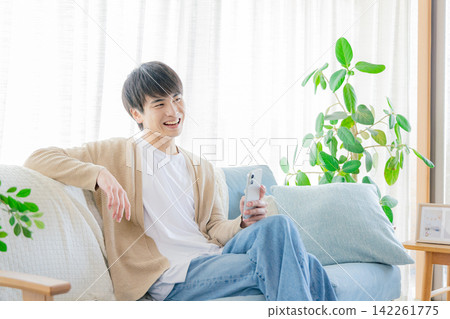 一個男人在客廳看著他的智慧型手機 一個男人在客廳看著他的智慧型手機 142261775
